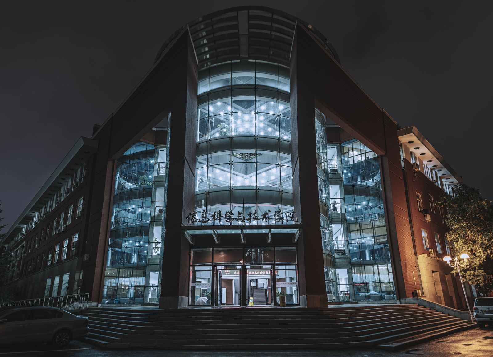 Illuminated modern building facade with glass features captured at night in an urban setting.