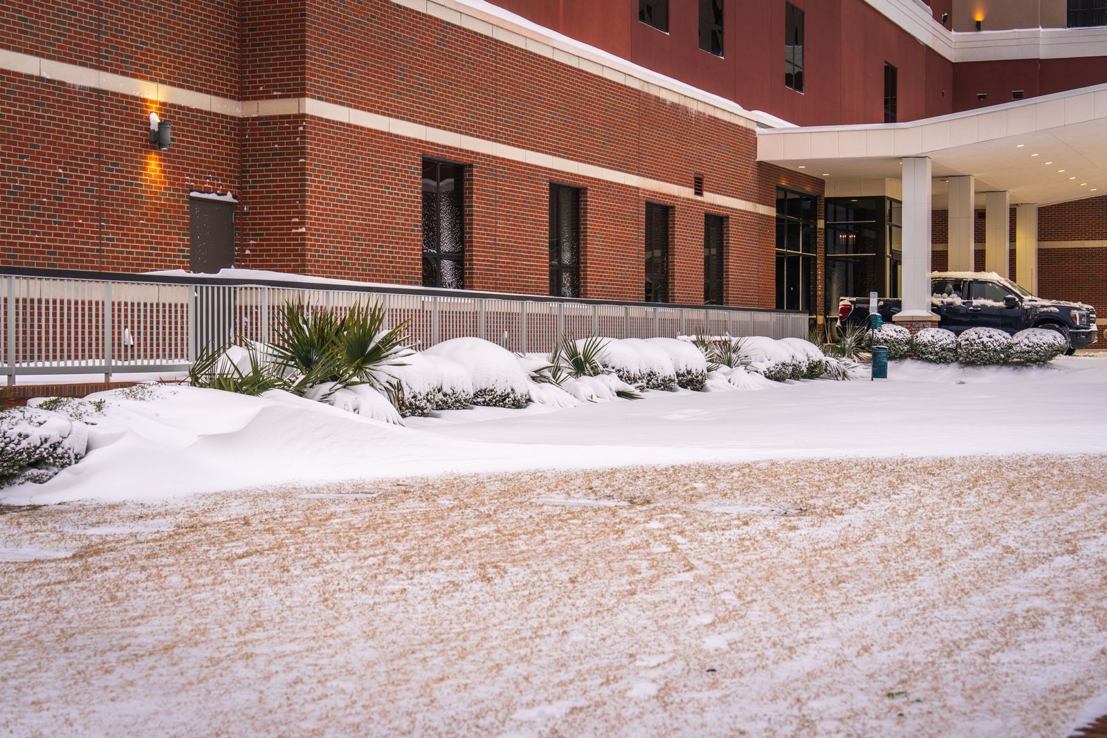 Snow blankets a modern brick building exterior during winter in a city setting.