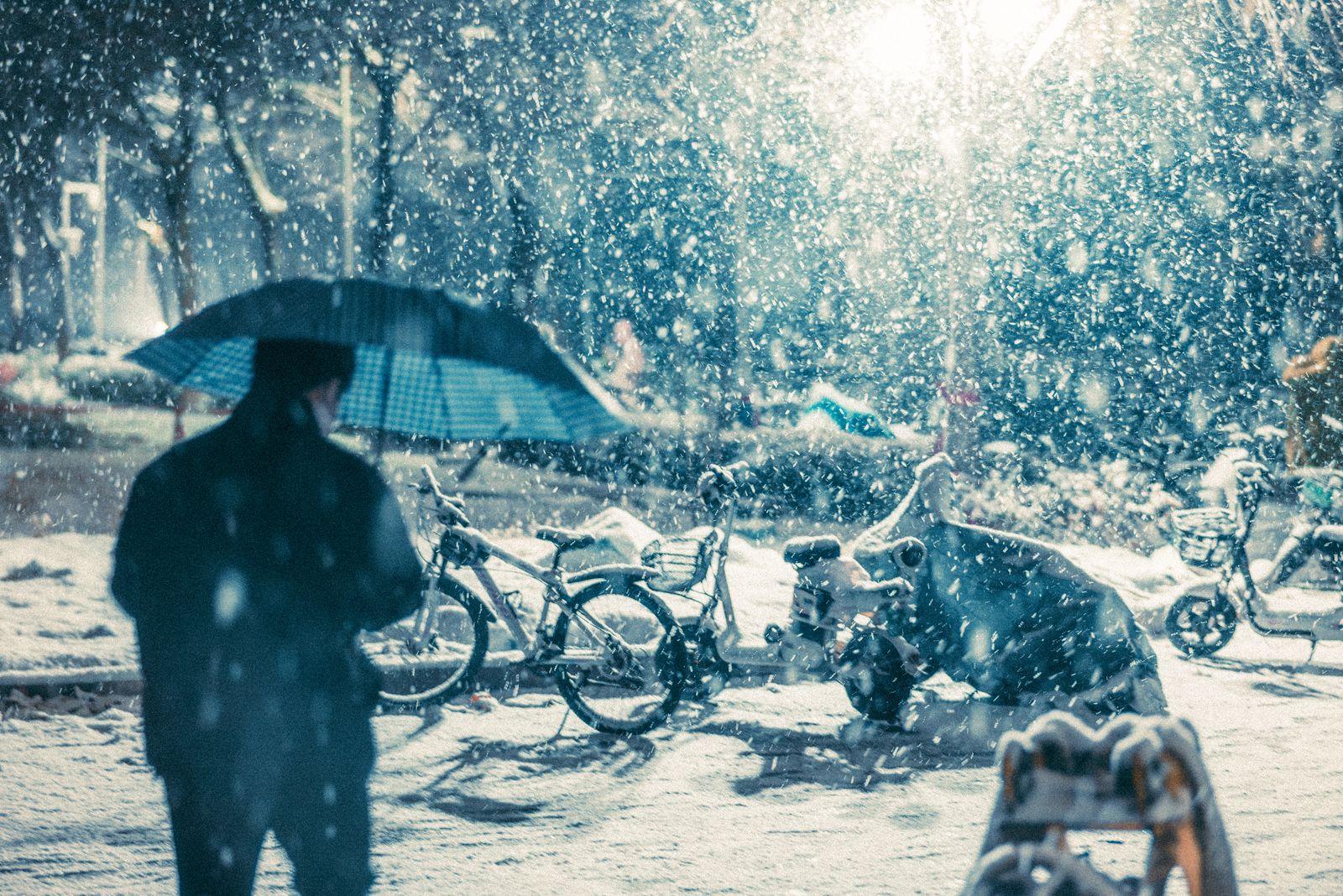 A snowy night scene with a person holding an umbrella near parked bicycles under streetlights.