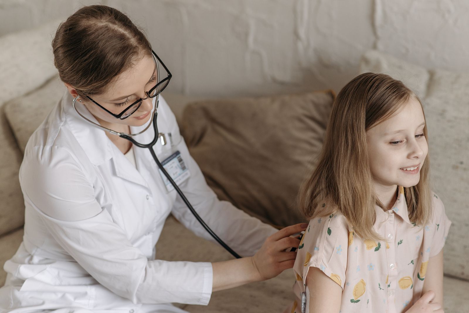 A doctor with a stethoscope examining a smiling girl during a medical check-up at home.