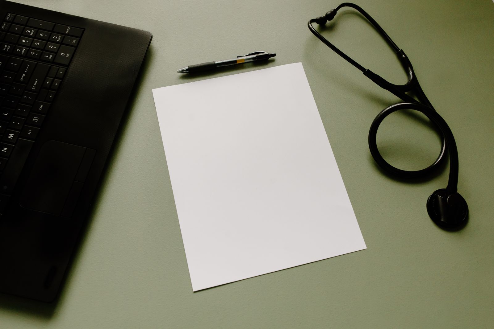 Professional workspace featuring a laptop, stethoscope, pen, and paper sheet for healthcare tasks.